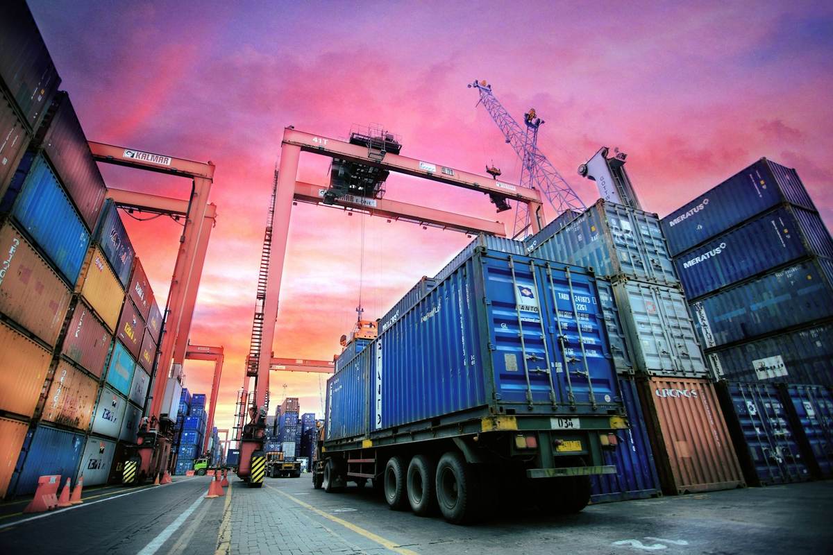 Gantry cranes and stacked shipping containers at a port terminal at sunset